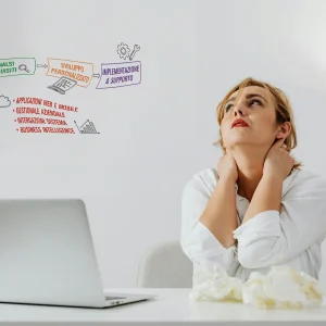 Una impiegata davanti ad un computer si preoccupa portando le mani al collo in segno di stanchezza.